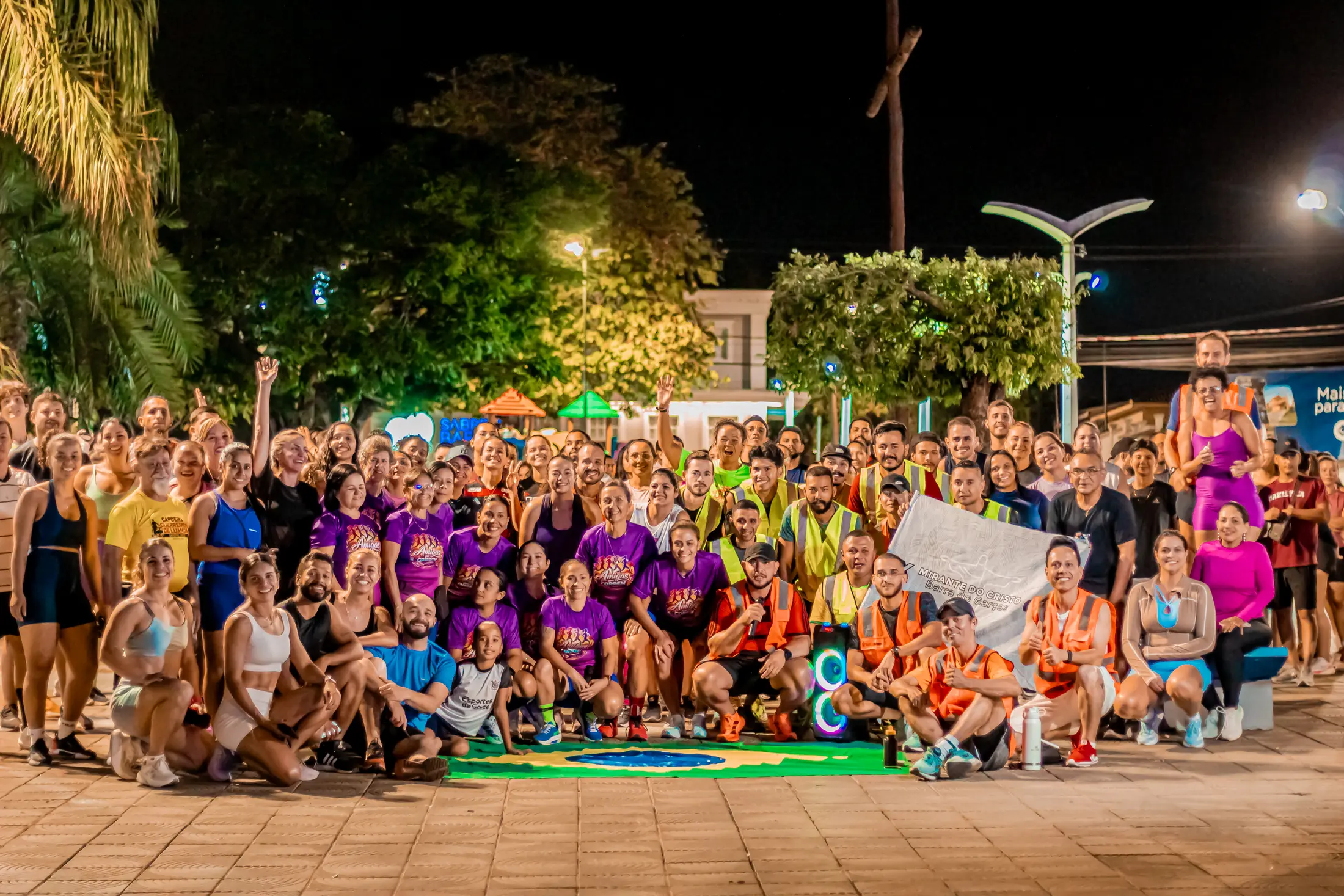 Grande grupo dos Miranteiros reunido à noite na praça com atletas, staff e batedores