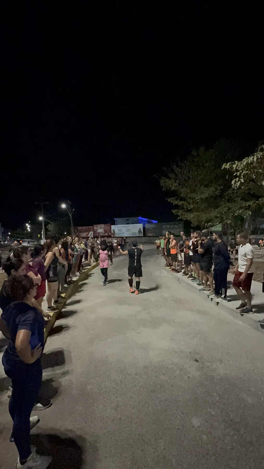 Duas filas de participantes formando um corredor durante o treino noturno