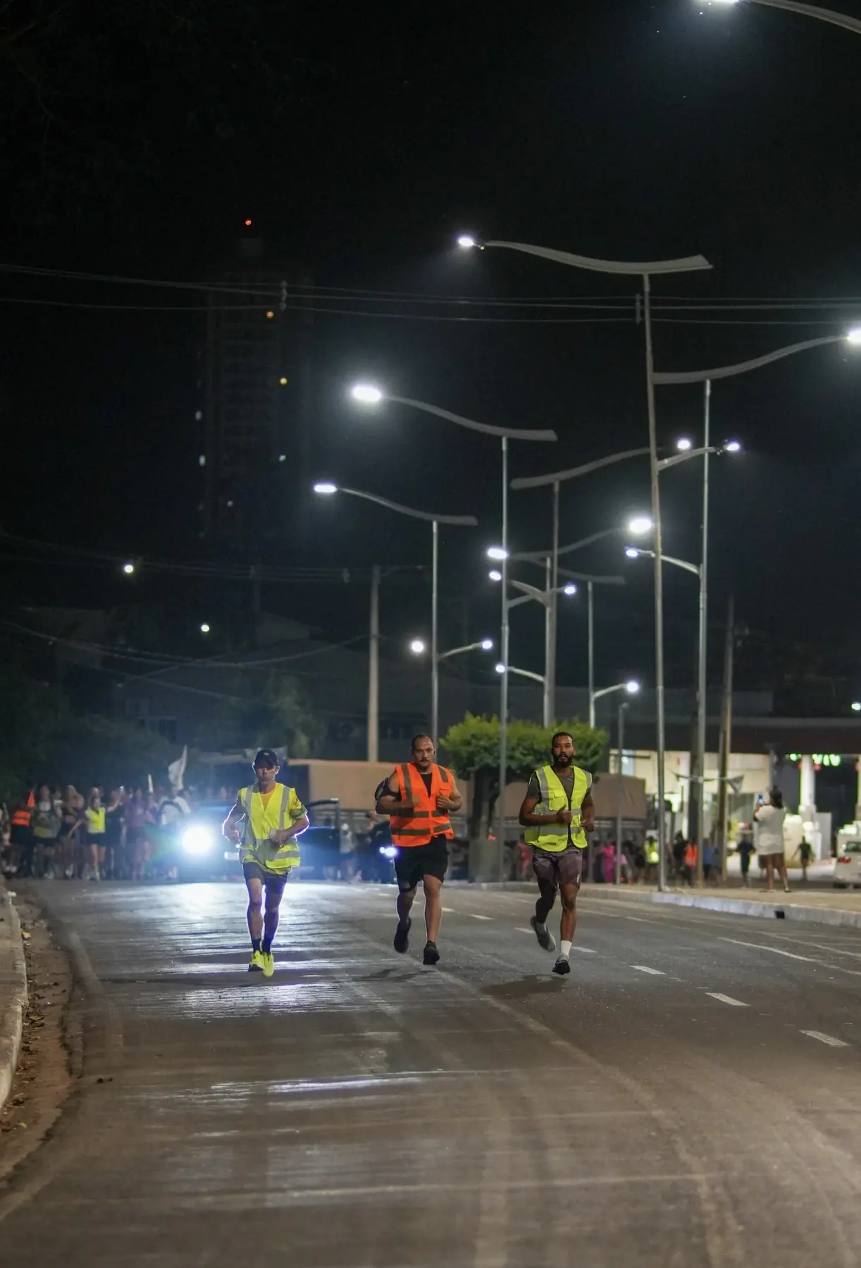 Três batedores dos Miranteiros correndo à frente do grupo em uma avenida iluminada