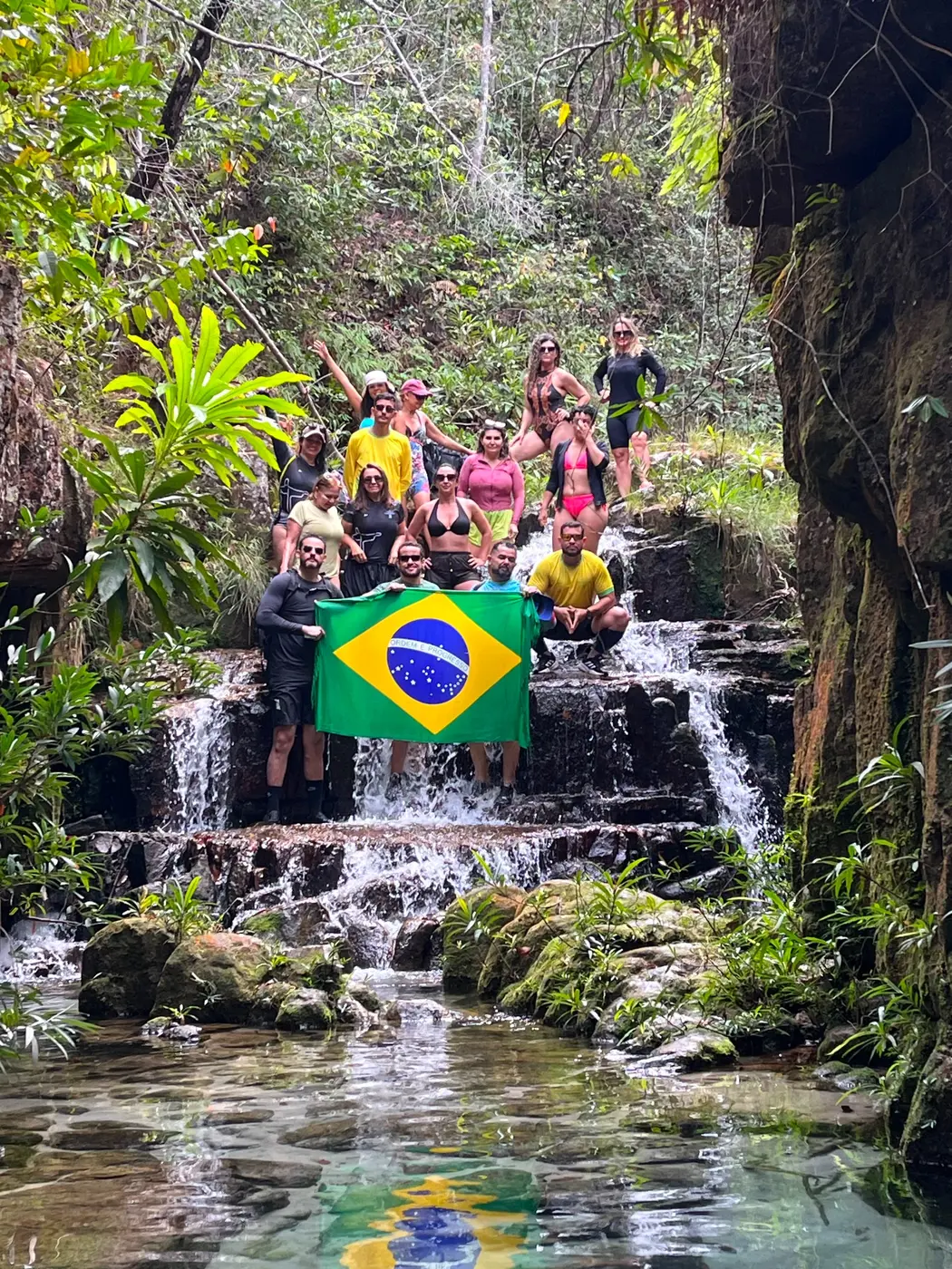 Grupo dos Miranteiros em uma cachoeira durante uma trilha com a bandeira do Brasil